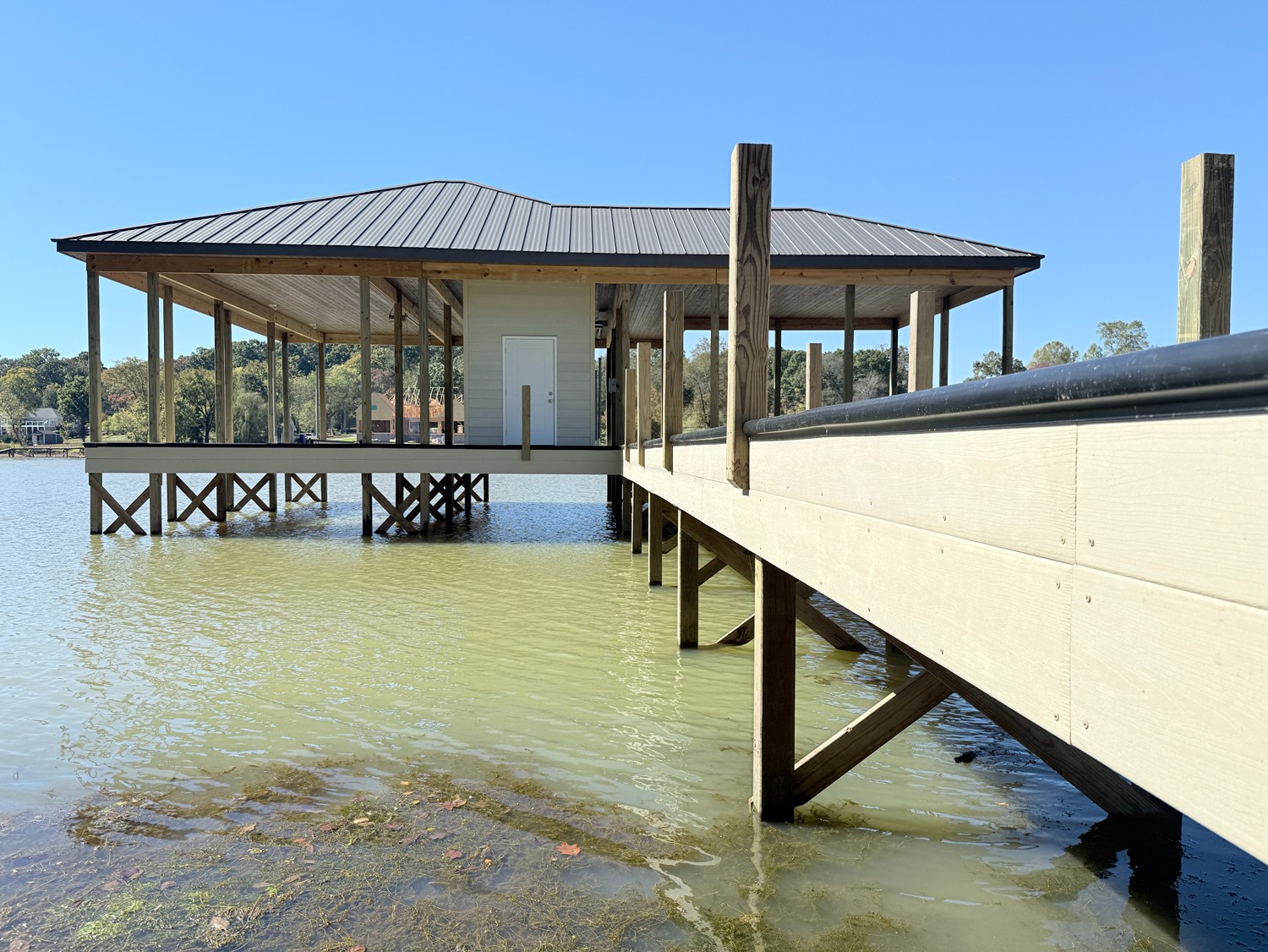 Covered boathouse with white siding and a long elevated walkway