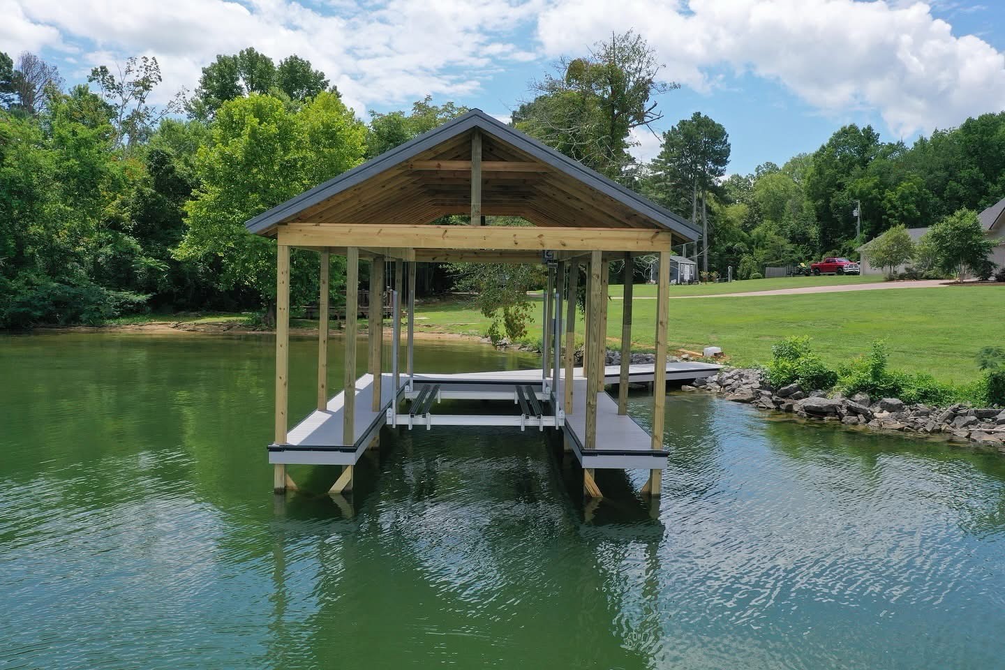 Gable-roof covered boat dock with composite decking on a green lake